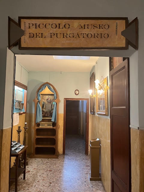 Entrada do Pequeno Museu do Purgatório, dentro da Igreja do Sagrado Coração do Sufrágio em Roma, com corredor e imagens religiosas expostas.