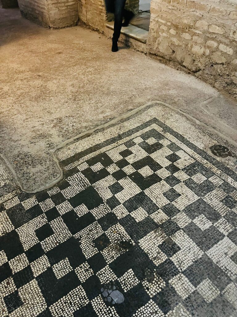 Detalhe de um piso de mosaico romano com desenhos geométricos em preto e branco, localizado no subterrâneo da Basílica de Santa Cecília.