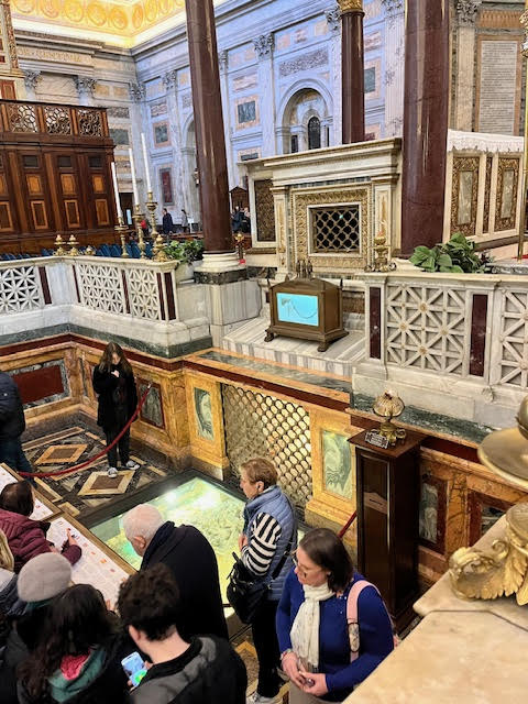 Cripta da Basílica de São Paulo Extramuros em Roma, com lápide do túmulo de São Paulo e urna contendo a corrente de seu martírio, rodeada por peregrinos durante o Jubileu 2025.