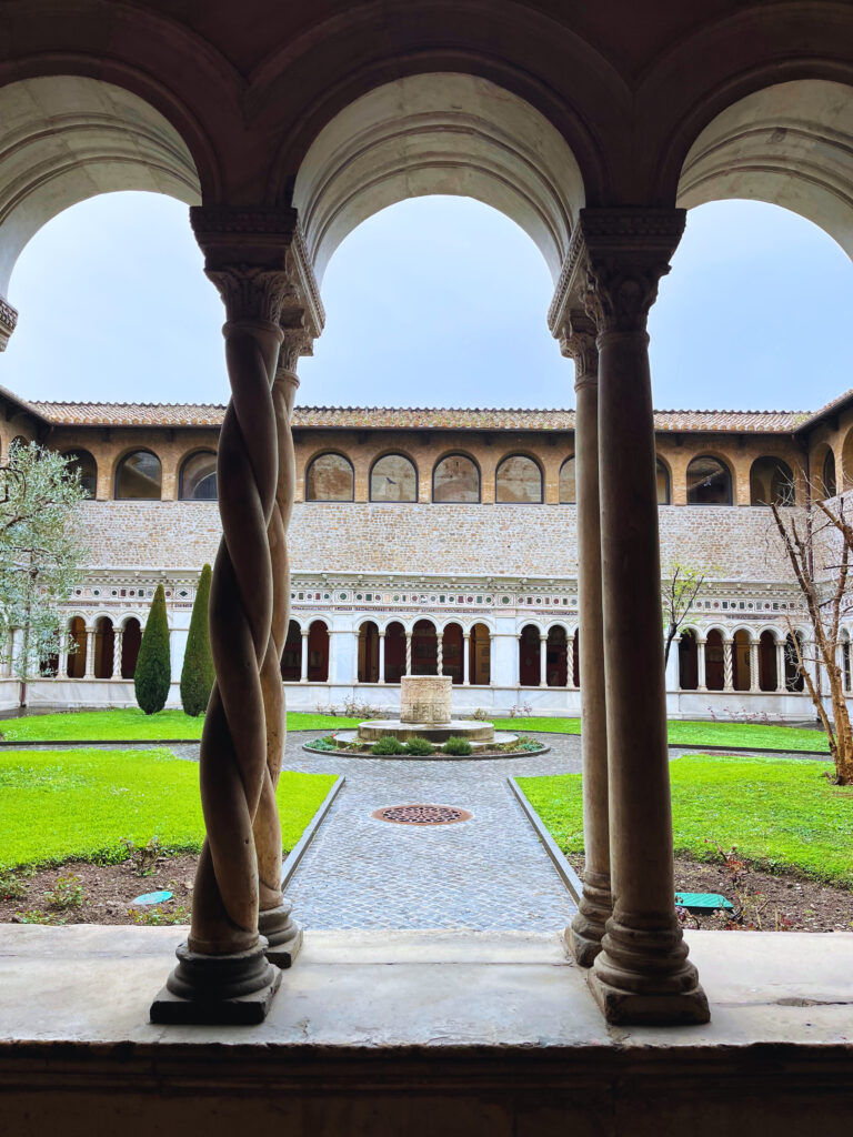 Claustro medieval da Basílica de São João de Latrão em Roma, com colunas retorcidas e jardim interno com poço antigo.