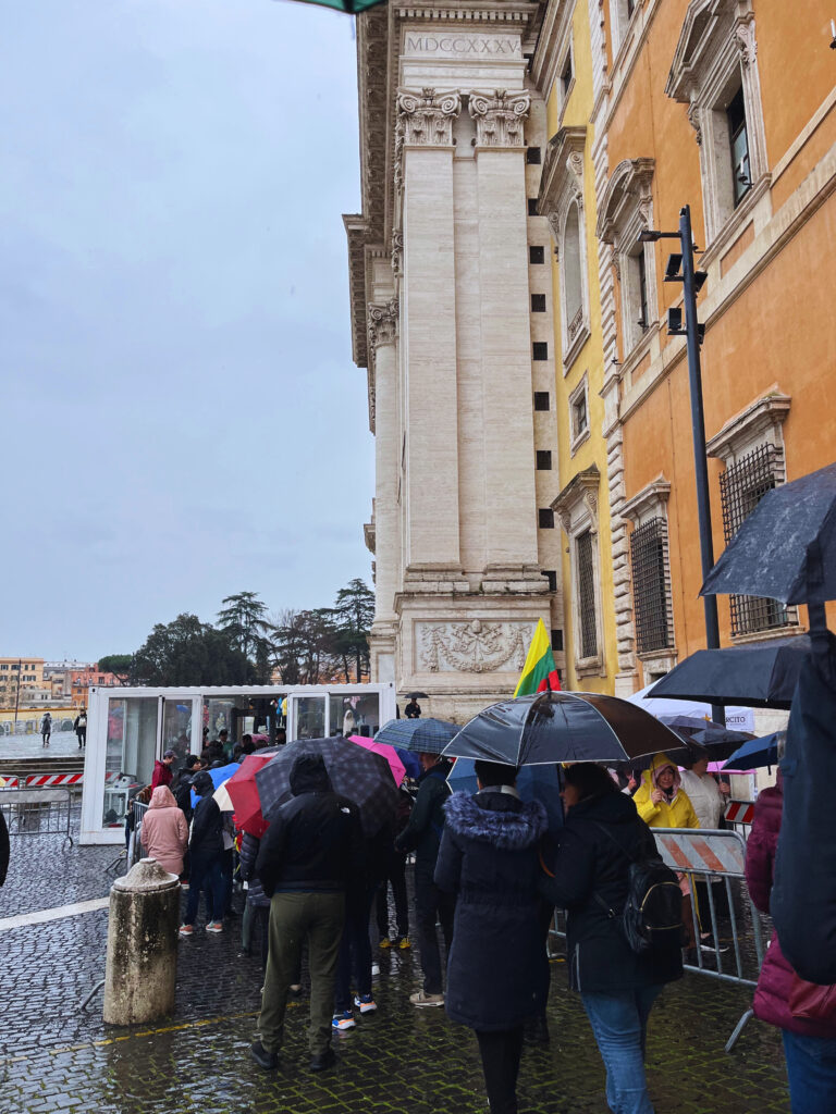 Fila de pessoas com guarda-chuvas antes do controle policial de entrada na Basílica de São João de Latrão em Roma, durante o Jubileu 2025.