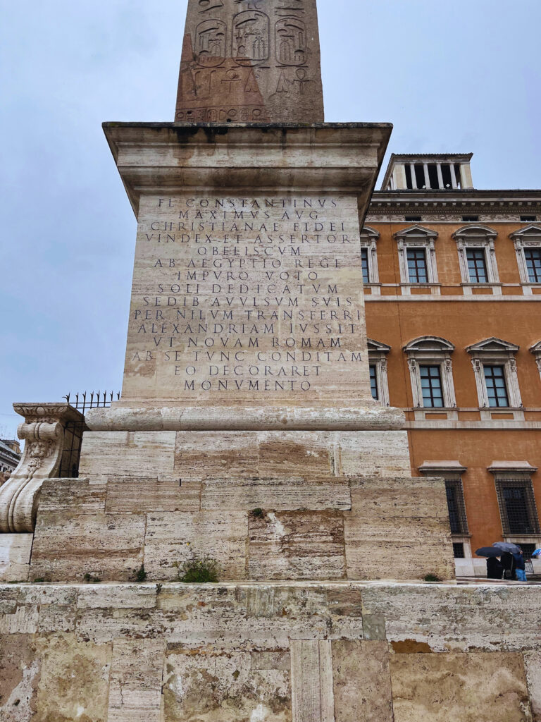 Inscrição em latim na base do obelisco Lateranense, próximo ao Batistério Lateranense, contando a história do transporte por Constantino e Constâncio II.
